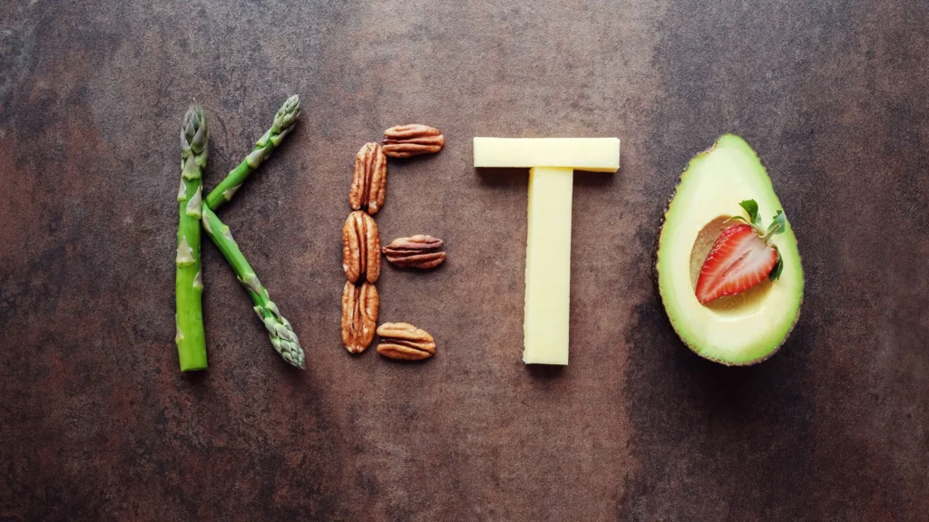 Palabra keto formada con alimentos saludables como espárragos, nueces, queso y aguacate con fresa, representando la dieta cetogénica.